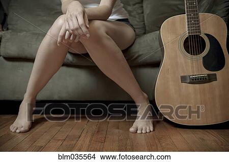 Picture - Legs of Caucasian woman sitting with guitar on sofa. Fotosearch