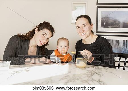 Lesbian couple feeding baby daughter at table View Large Photo Image Stock Image - Lesbian couple feeding baby daughter at table. Fotosearch