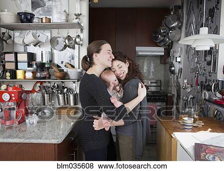 Lesbian couple hugging baby daughter in kitchen View Large Photo Image Stock Photo - Lesbian couple hugging baby daughter in kitchen. Fotosearch