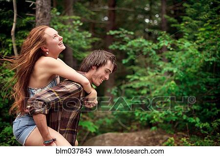 Stock Image - Man carrying girlfriend piggyback in forest. Fotosearch