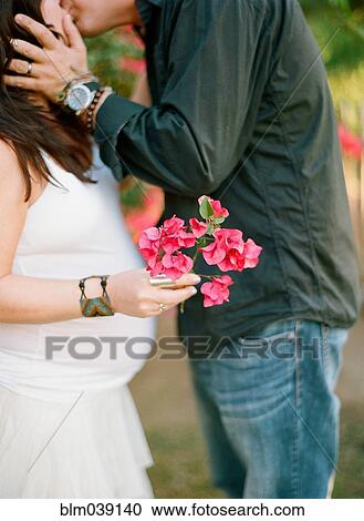 Stock Image - Man kissing pregnant wife outdoors. Fotosearch