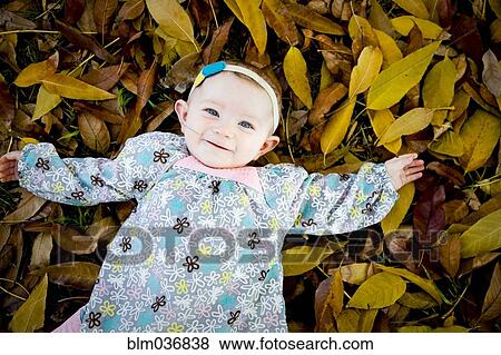 Stock Photo - Mixed race baby girl laying in autumn leaves. Fotosearch