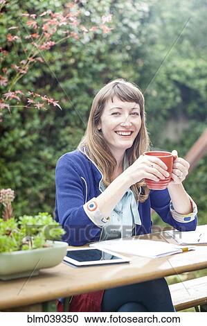 Stock Image - Mixed race businesswoman drinking coffee in backyard. Fotosearch