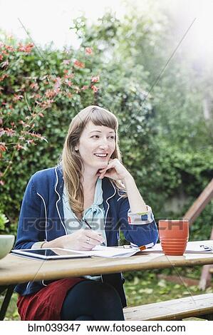 Stock Photo - Mixed race businesswoman writing notes in backyard. Fotosearch