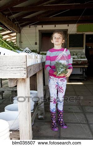 Stock Photo - Mixed race girl holding bag of produce in farmers market. Fotosearch