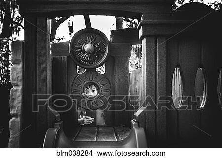 Picture - Mixed race girl peering through play structure in park. Fotosearch