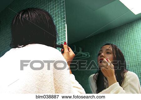 Stock Photo - Mixed race woman applying makeup in mirror. Fotosearch