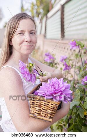 Stock Image - Mixed race woman picking flowers in garden. Fotosearch