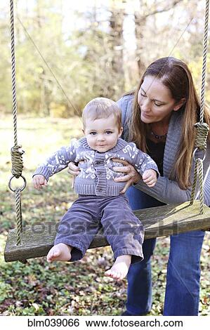 Stock Photograph - Mother and baby son on swing in backyard. Fotosearch