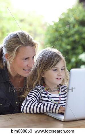 Stock Image - Mother and daughter using laptop at table. Fotosearch