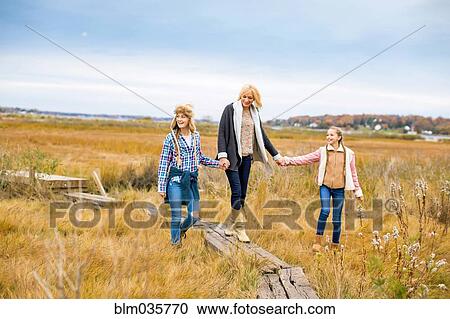 Stock Image - Mother and daughters walking in rural field. Fotosearch