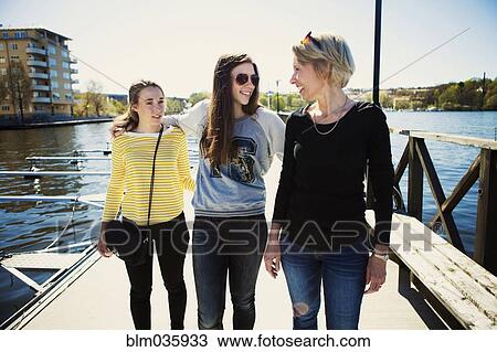 Stock Image - Mother and daughters walking on dock in harbor. Fotosearch