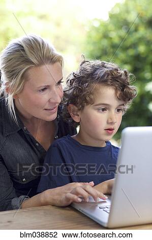 Stock Image - Mother and son using laptop at table. Fotosearch