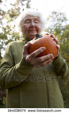 Picture - Older Caucasian woman admiring pumpkin outdoors. Fotosearch
