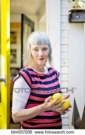 Stock Photograph - Older Caucasian woman holding lemons outdoors. Fotosearch