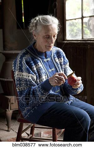 Stock Photo - Older Caucasian woman peeling fruit in living room. Fotosearch