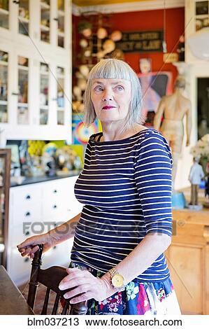 Stock Image - Older Caucasian woman standing at kitchen table. Fotosearch