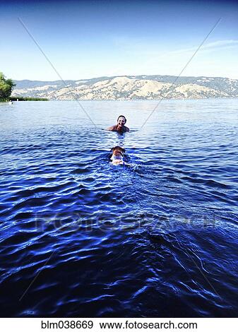 Stock Photo - Older Caucasian woman swimming with dog in remote lake. Fotosearch