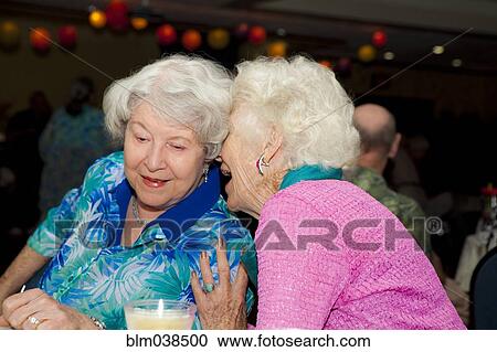 Stock Image - Older Caucasian women whispering at party in retirement home. Fotosearch