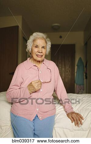 Stock Photo - Older mixed race woman sitting on bed. Fotosearch