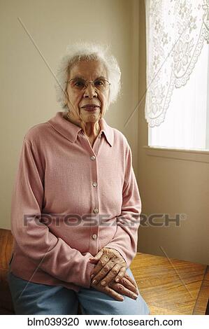 Stock Image - Older mixed race woman sitting on table. Fotosearch