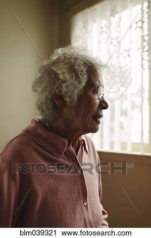 Stock Image - Older mixed race woman standing at window. Fotosearch
