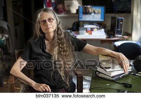 Stock Photography - Older woman leaning on stack of books at desk. Fotosearch