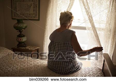 Stock Photograph - Pensive older woman looking out bedroom window. Fotosearch