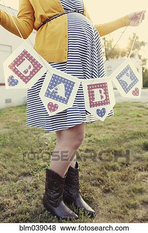 Stock Photo - Pregnant Caucasian woman holding baby banner in backyard. Fotosearch