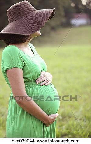 Picture - Pregnant Caucasian woman holding belly in field. Fotosearch