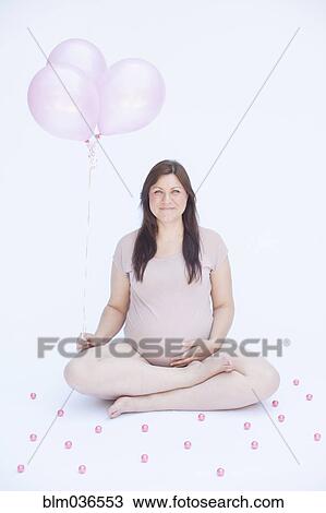 Stock Image - Pregnant Caucasian woman holding bunch of balloons. Fotosearch