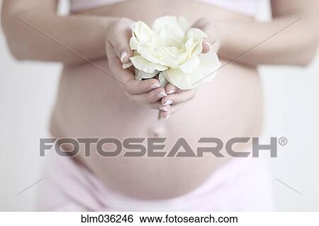 Stock Photograph - Pregnant Caucasian woman holding flower. Fotosearch