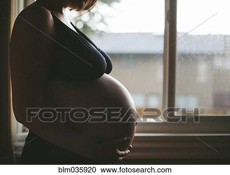 Stock Image - Pregnant Caucasian woman standing at window. Fotosearch