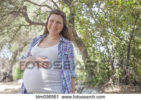 Stock Image - Pregnant Caucasian woman standing in park. Fotosearch