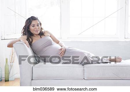 Pregnant Hispanic woman holding belly on sofa View Large Photo Image Stock Photo - Pregnant Hispanic woman holding belly on sofa. Fotosearch