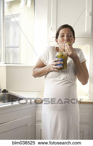 Stock Photography - Pregnant woman eating pickles in kitchen. Fotosearch