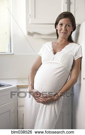 Stock Photograph - Pregnant woman holding her belly in kitchen. Fotosearch