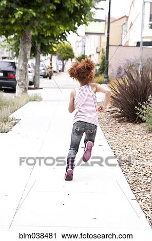 Stock Image - Rear view of girl running on city sidewalk. Fotosearch
