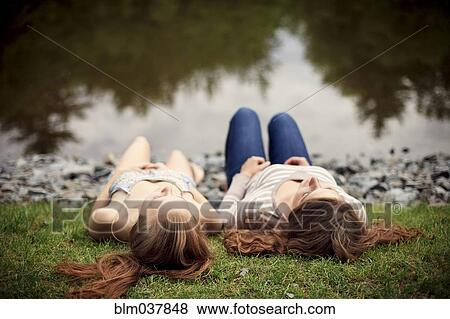 Stock Photo - Rear view of girls laying near lake. Fotosearch