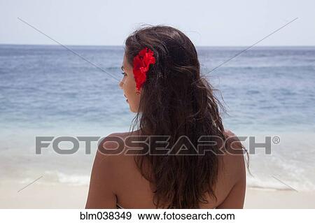 Stock Photo - Rear view of woman wearing flower in her hair on beach. Fotosearch