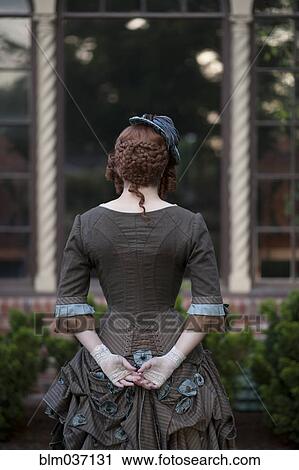 Stock Image - Rear view of woman wearing vintage gown and hat. Fotosearch