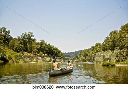 Stock Image - Rear view of women rowing canoe in rural lake. Fotosearch