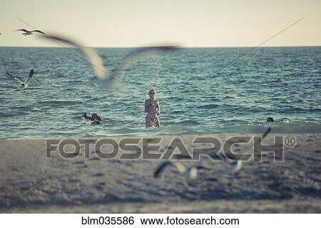 Stock Photograph - Seagulls flying near Caucasian teenage girl standing in ocean. Fotosearch