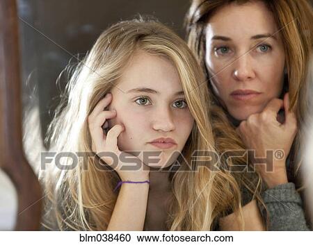 Stock Image - Serious mother and daughter examining themselves in mirror. Fotosearch