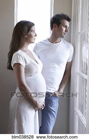 Stock Photo - Serious pregnant couple looking out window. Fotosearch