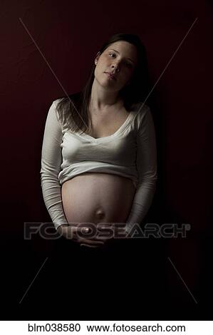 Stock Image - Serious pregnant woman holding her belly. Fotosearch