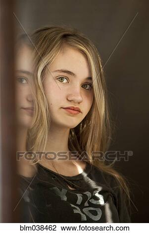 Stock Image - Serious teenage girl examining herself in mirror. Fotosearch