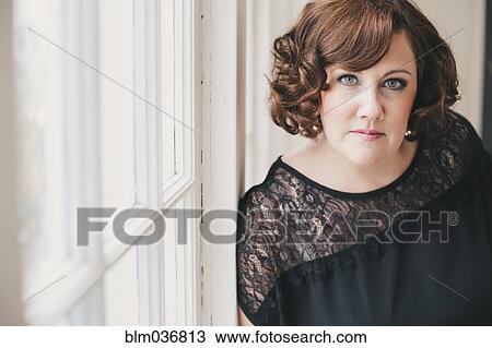Stock Image - Serious woman leaning on window. Fotosearch