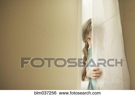 Stock Photograph - Shy Caucasian girl peeking around curtain. Fotosearch