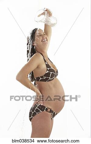 Picture - Side view of pregnant woman pouring water on herself. Fotosearch